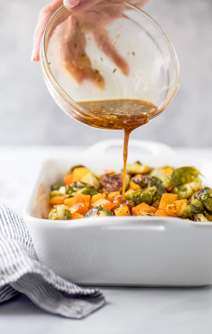 pouring maple dijon glaze over roasted butternut squash and brussel sprouts