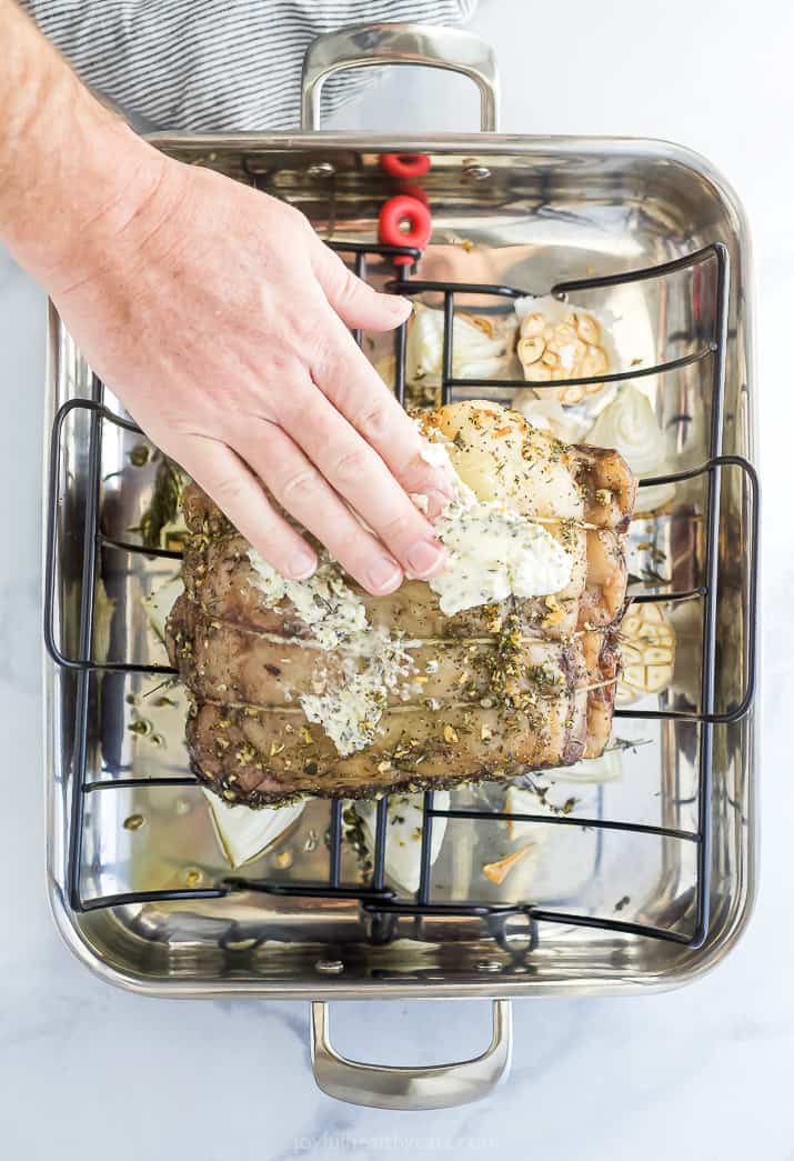 Hand rubbing herbed butter onto prime rib roast.