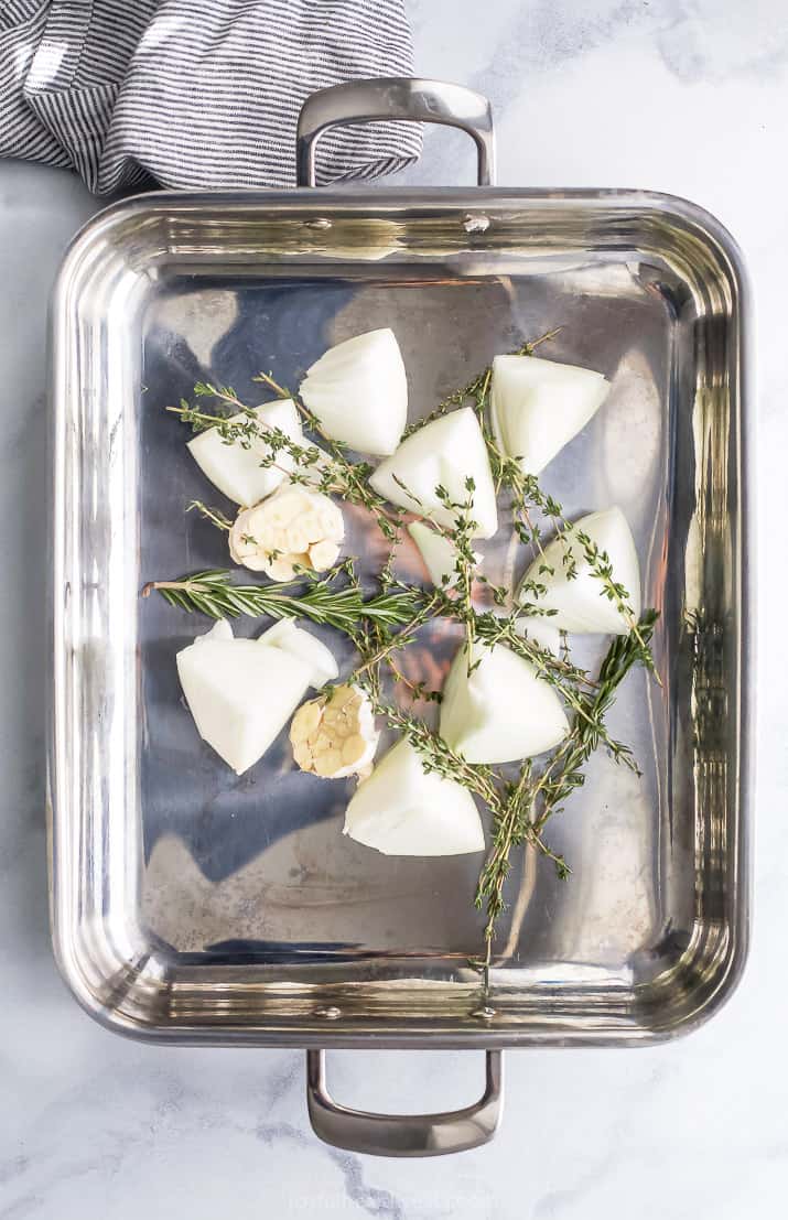 Onions, garlic, and herbs in roasting pan.
