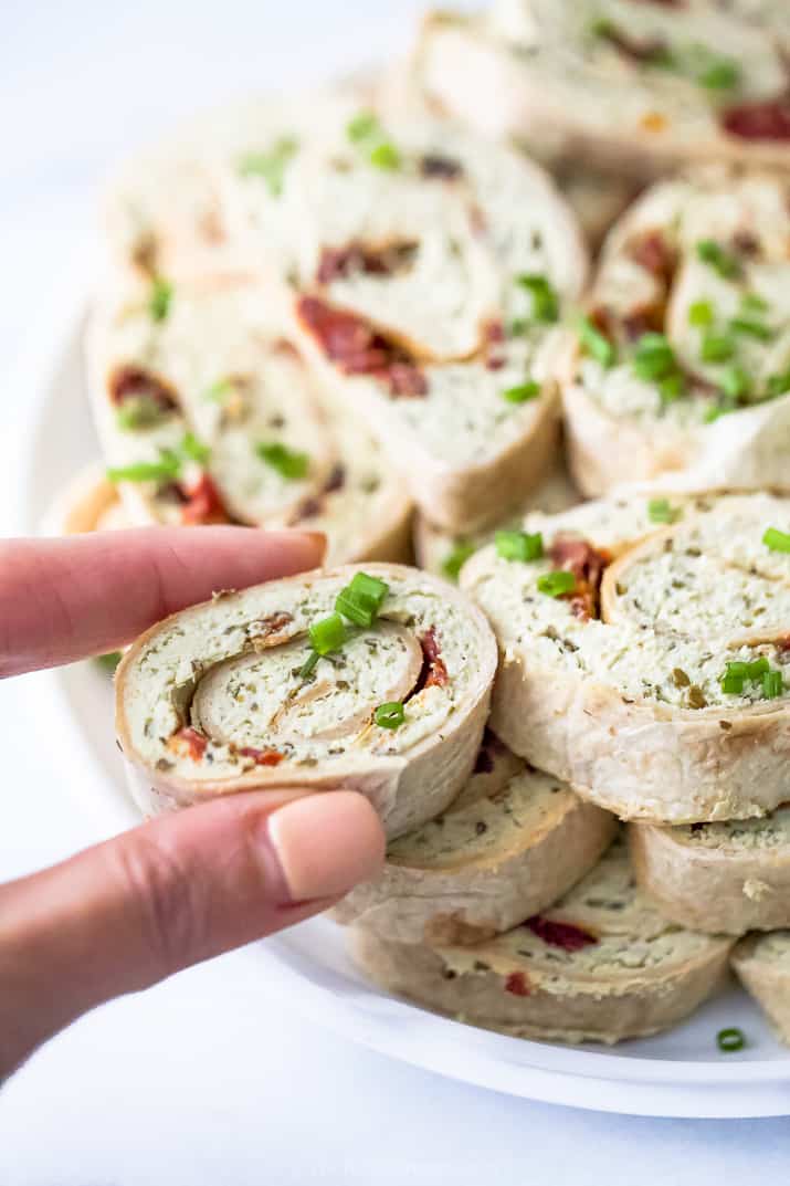 a hand taking one roll of a pesto chicken pinwheel