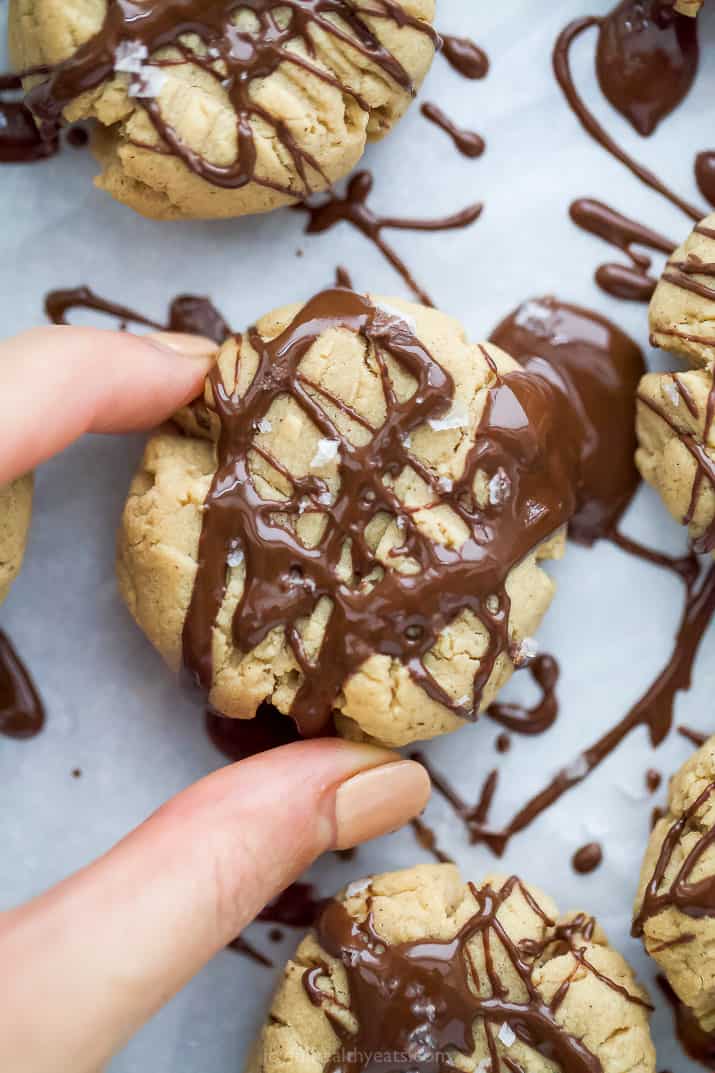 a hand holding vegan peanut butter cookies with a chocolate drizzle