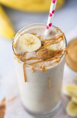 Peanut butter banana smoothie in a glass with more peanut butter and a banana slice on top.