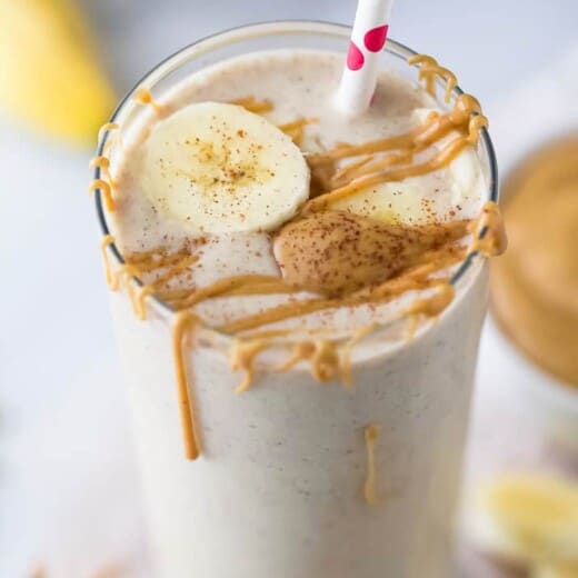 Peanut butter banana smoothie in a glass with more peanut butter and a banana slice on top.