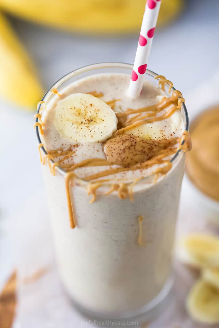 Peanut butter banana smoothie in a glass with more peanut butter and a banana slice on top.