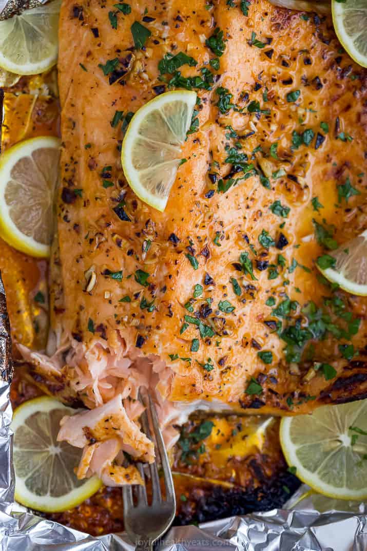 Flaky baked salmon with a fork in it, topped with lemon slices