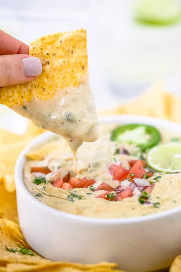 A hand dipping a chip into a bowl of white queso dip.
