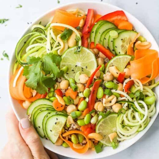 hand holding a bowl of vegetarian thai quinoa salad topped with peanut dressing