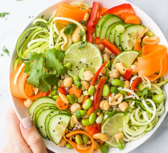 hand holding a bowl of vegetarian thai quinoa salad topped with peanut dressing
