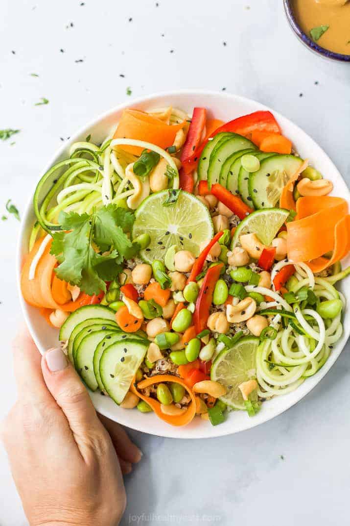 hand holding a bowl of vegetarian thai quinoa salad topped with peanut dressing