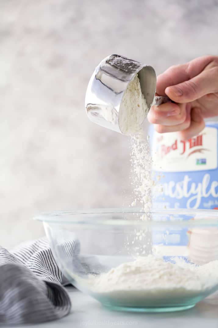 a measuring cup pouring pancake mix into a bowl