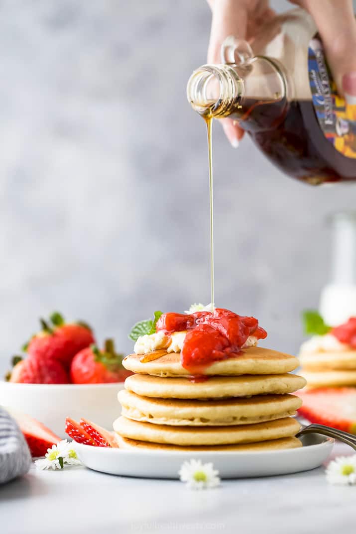 syrup being poured on top of fluffy pancakes with strawberry compote on top