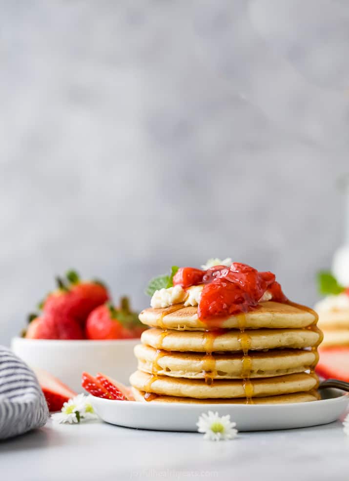 closeup of a fluffy pancake recipe with strawberry compote and syrup dripping down