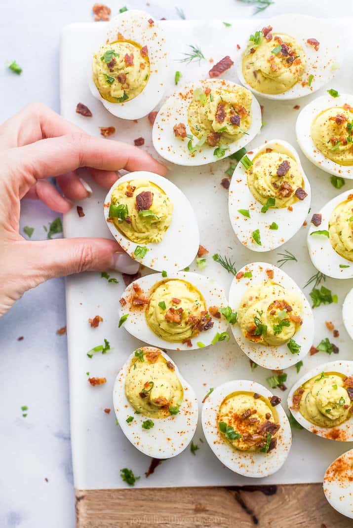 a hand grabbed a classic deviled egg with bacon