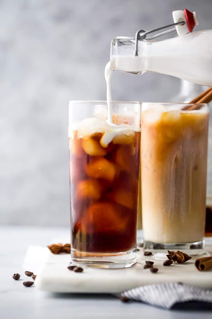 pouring coconut milk into an iced chai tea latte cup