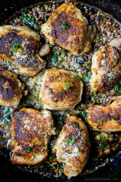 skilet garlic parmesan chicken thigns in a pan topped with fresh herbs
