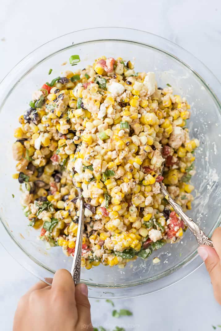 a bowl of esquites salad being tossed together