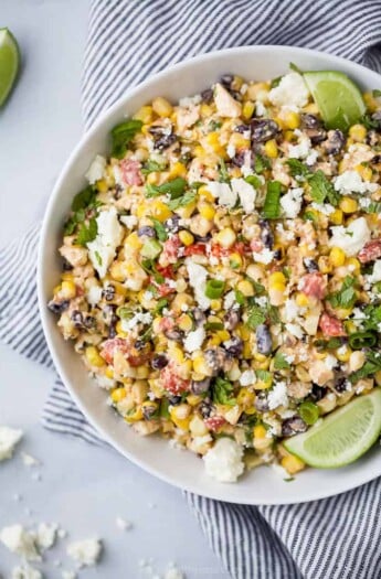 a bowl filled with grilled mexican street corn salad topped with limes