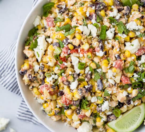 a bowl filled with grilled mexican street corn salad topped with limes