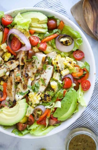 a bowl filled with a grilled honey mustard chicken salad with avocado and veggies