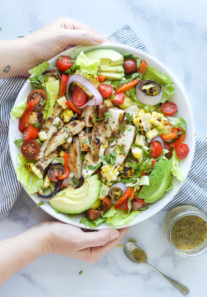 hands holding a bowl filled with grilled honey mustard chicken salad with avocado