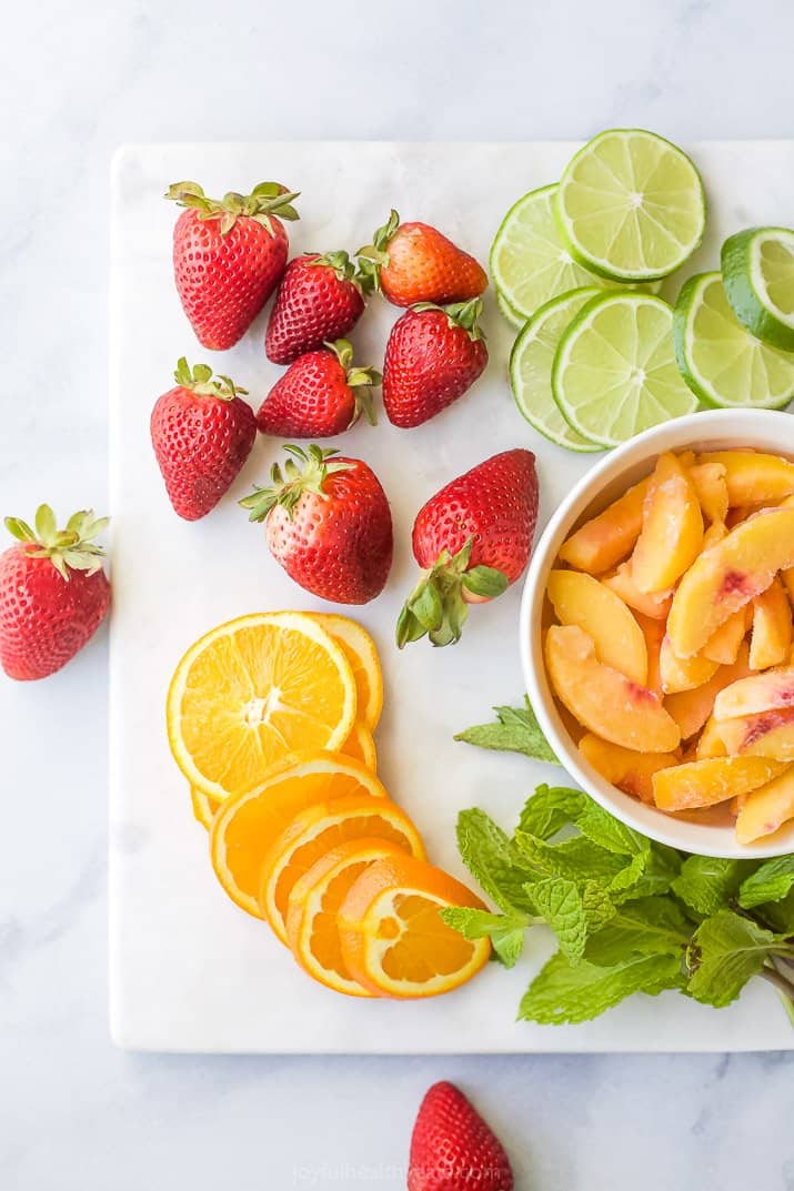 strawberries, peaches, lime and oranges on a cutting board with mint