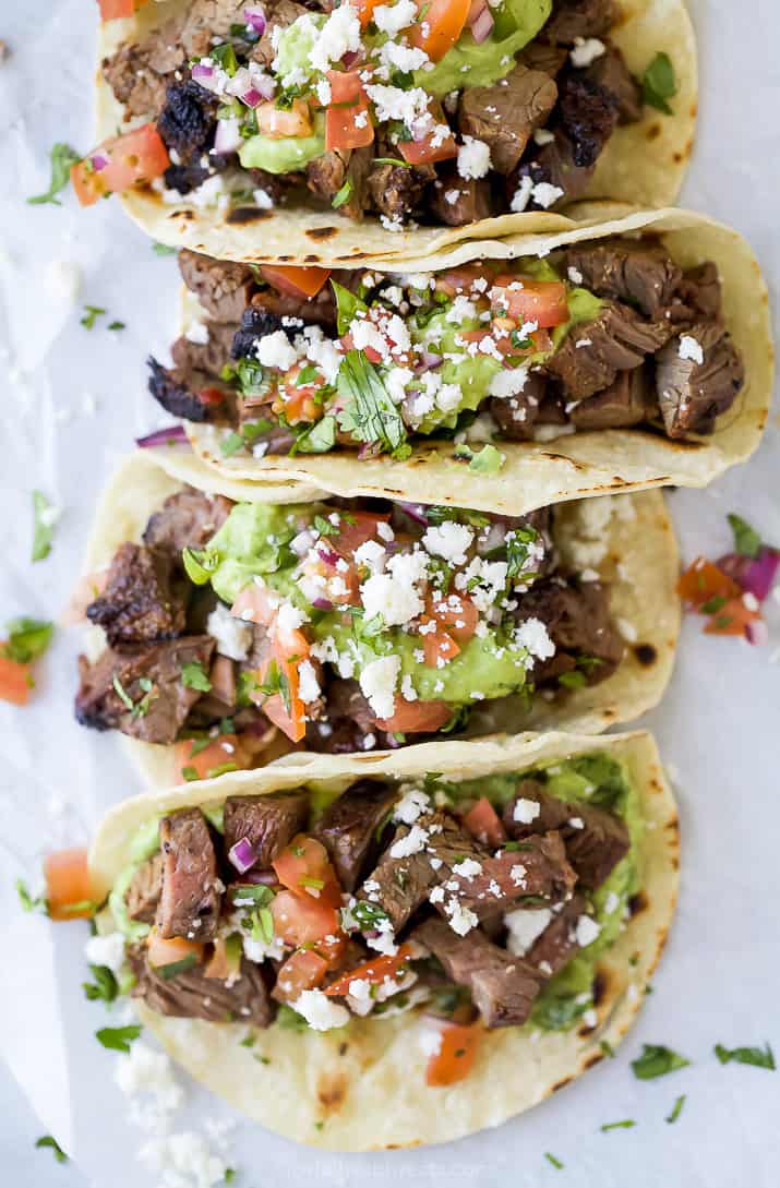 four best ever marinated carne asada tacos bunched up together and topped with pico de gallo and avocado crema