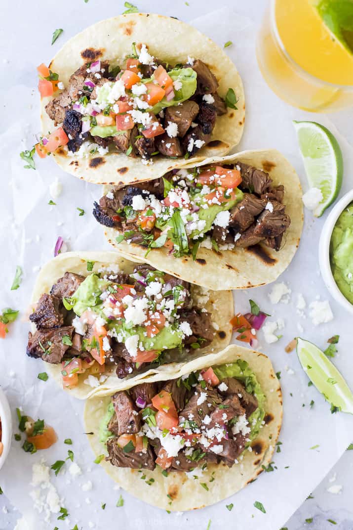 overhead photo of four corn tacos filled with marinated carne asada meat with avocado crema