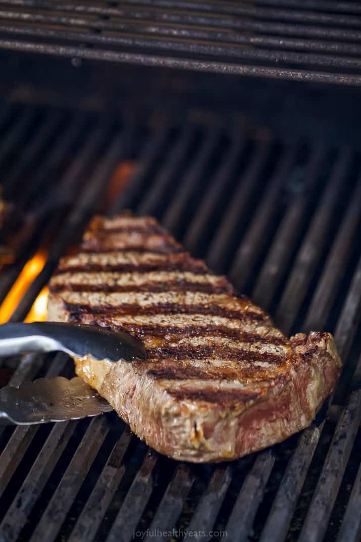 ribeye steak being grilled and held by tongs