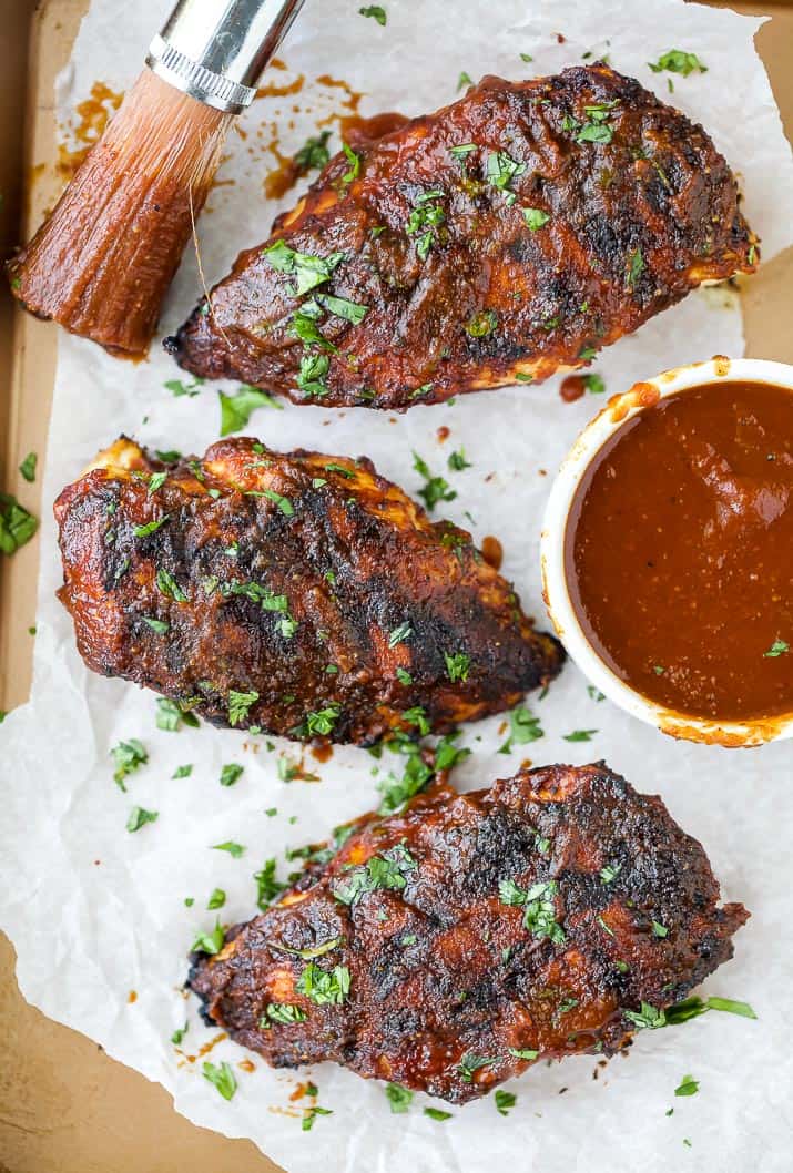 a bunch of bbq chickens on a baking sheet with a bbq sauce filled brush
