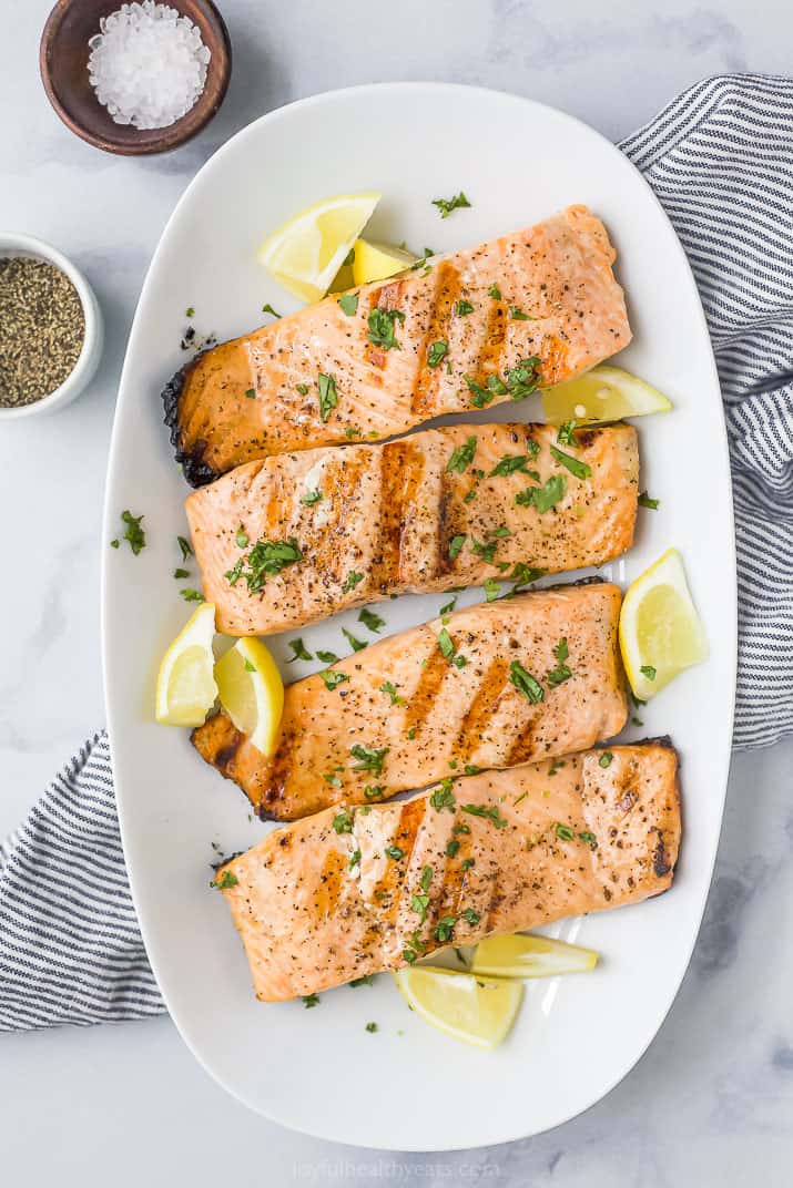 grilled salmon on a plate topped with lemon slices and fresh herbs