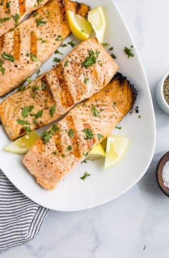 grilled salmon on a plate topped with lemon and fresh herbs