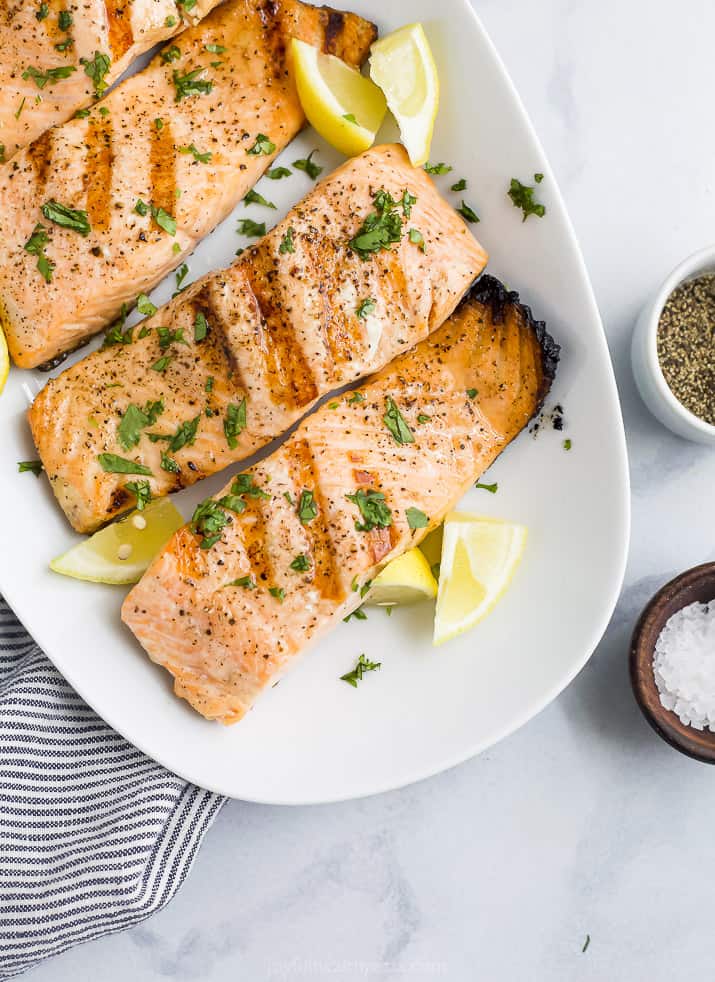 grilled salmon on a plate topped with lemon and fresh herbs