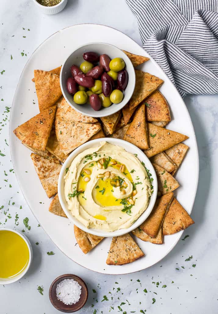 A bowl of hummus next to pita chips and olives
