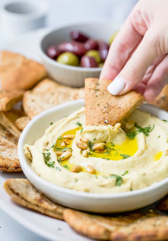 hand dipping a baked pita chips in homemade hummus