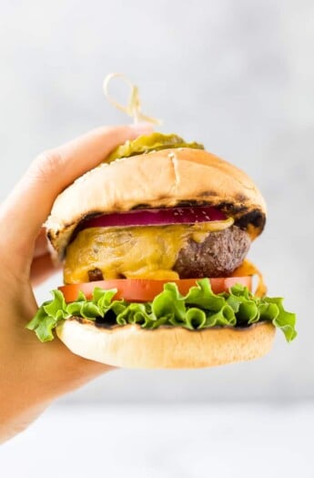 hands holding the best grilled burger topped with lettuce tomato onion and pickles
