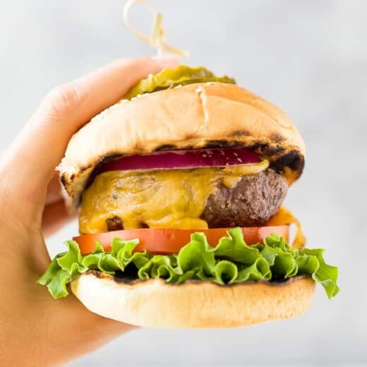 hands holding the best grilled burger topped with lettuce tomato onion and pickles