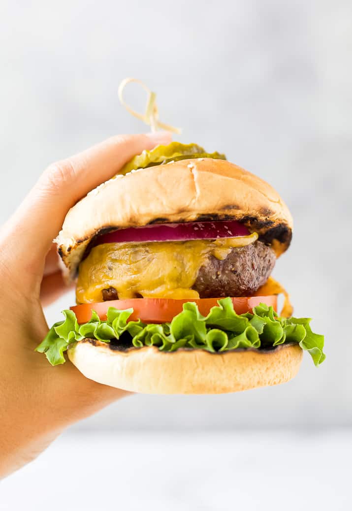 hands holding the best grilled burger topped with lettuce tomato onion and pickles