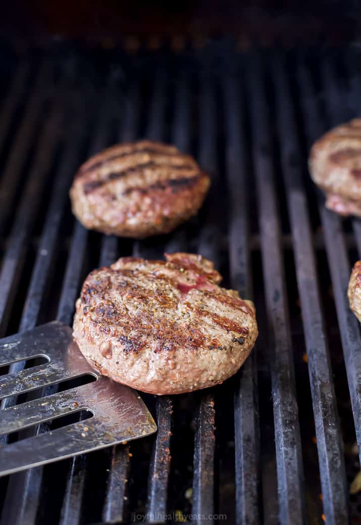 burgers being grilled on a gas grill with a spatula getting ready to flip