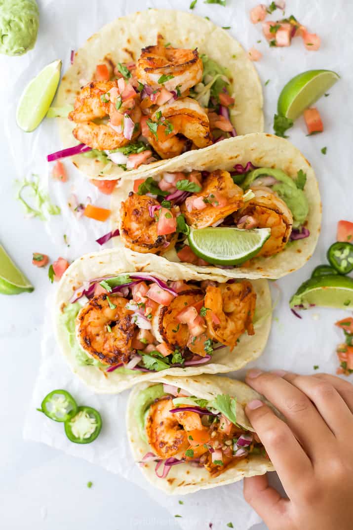 a hand grabbing a taco filled with shrimp and cabbage slaw