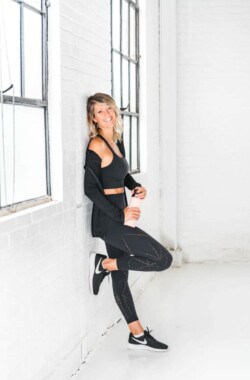 A woman in exercise clothes leaning against a gym wall