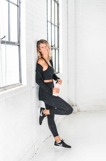 A woman in exercise clothes leaning against a gym wall