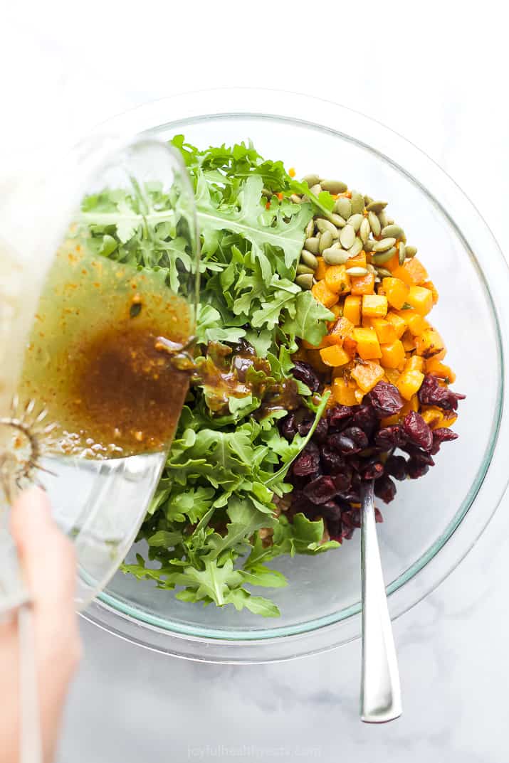 pouring dressing into a bowl with farro and arugula