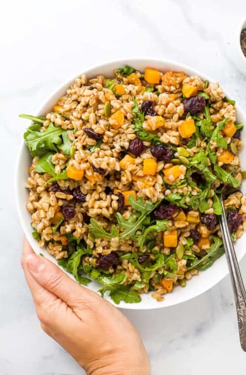 hand holding a bowl filled with farro salad