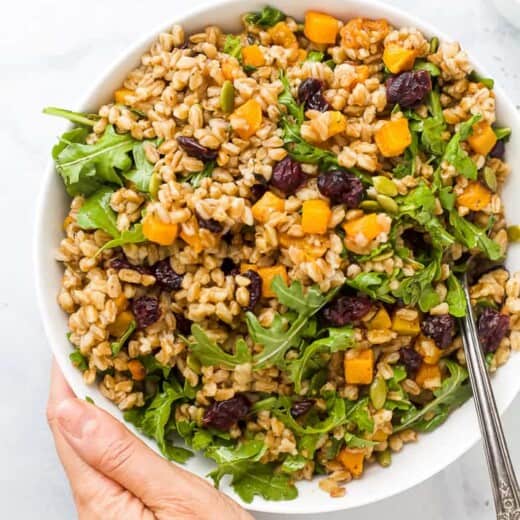 hand holding a bowl filled with farro salad