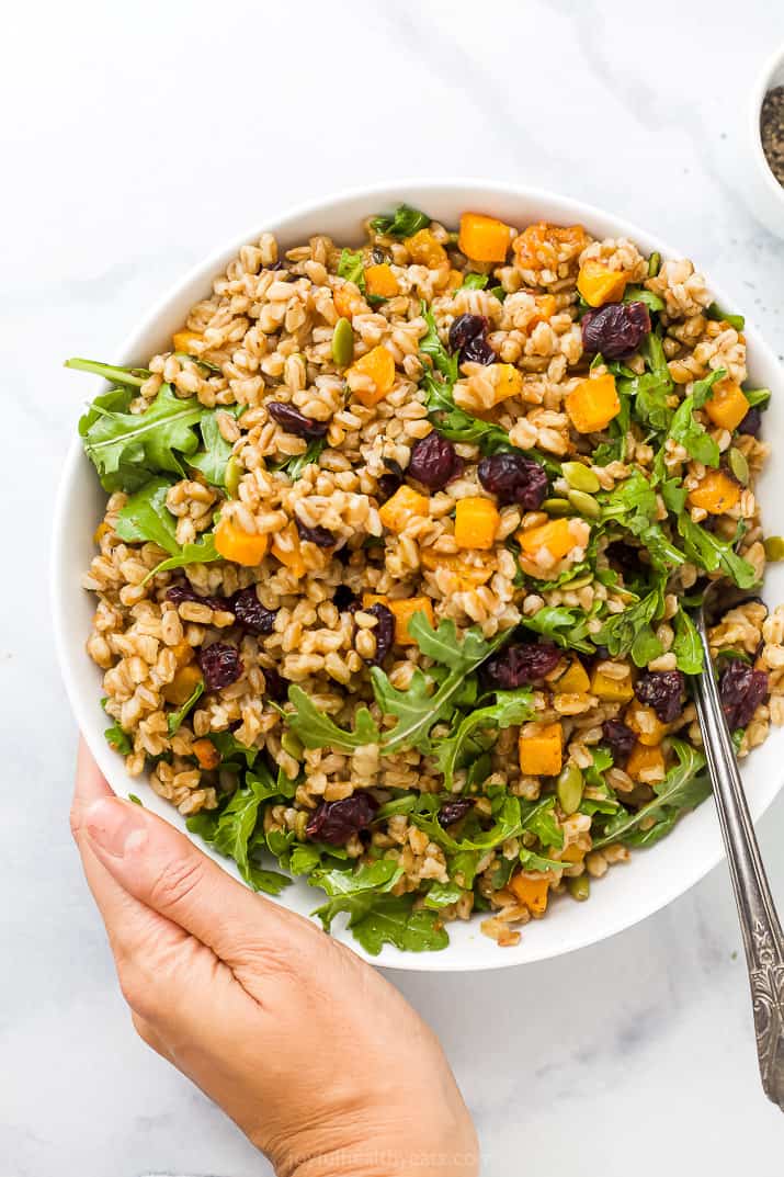 hand holding a bowl filled with farro salad