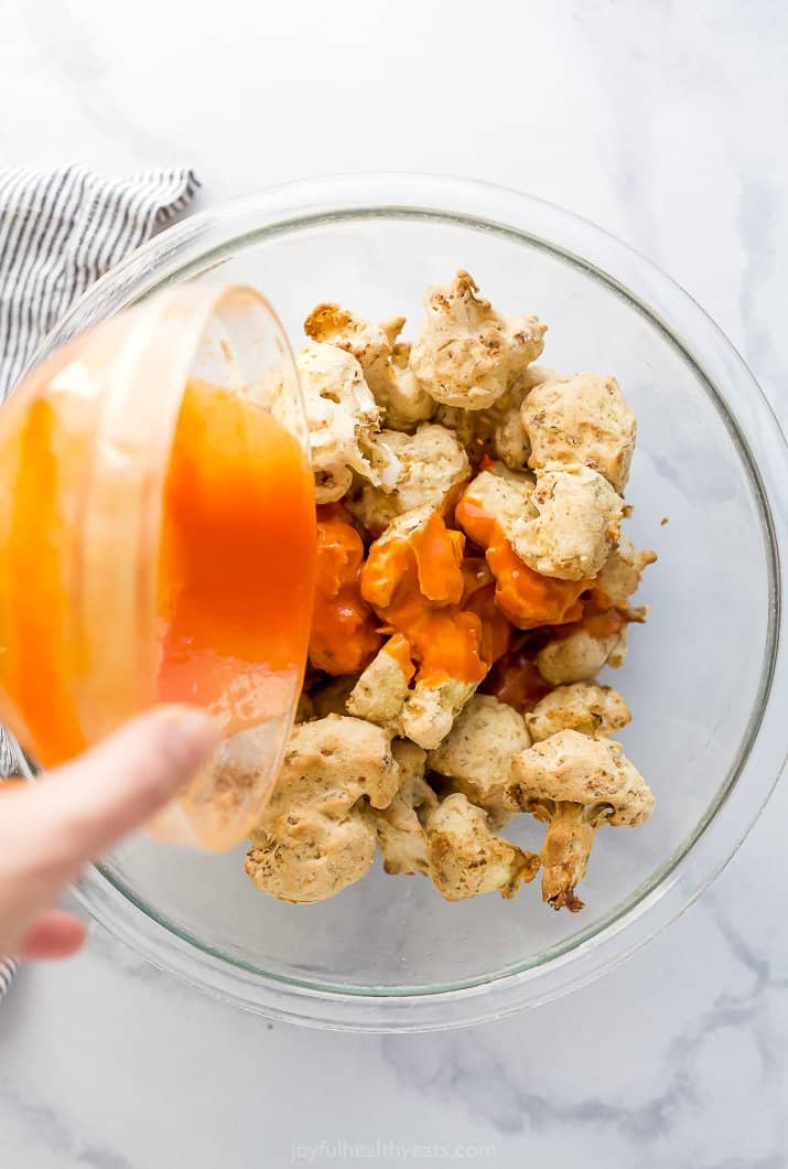 A Bowl of Buffalo Sauce Being Poured Over the Cauliflower Wings