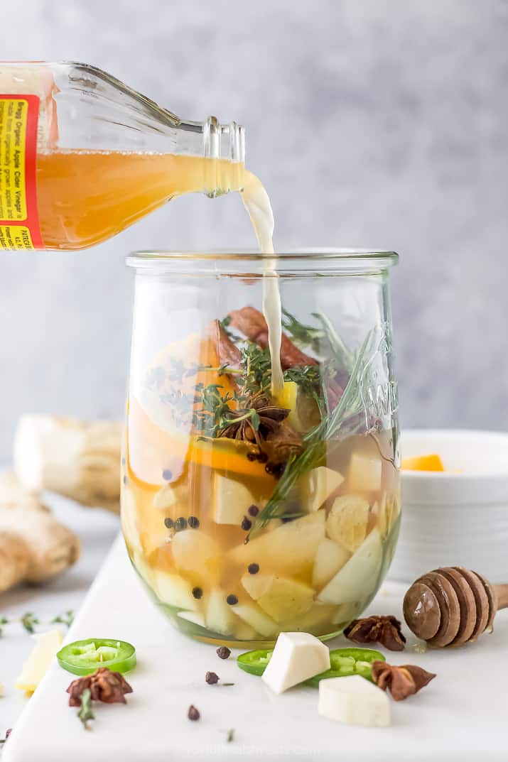 pouring apple cider vinegar into a mason jar filled with fire cider ingredients