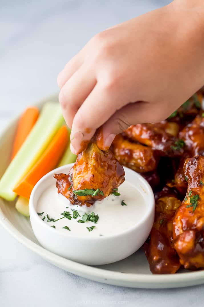 A Hand Dunking a Barbecue Wing in Ranch Dressing