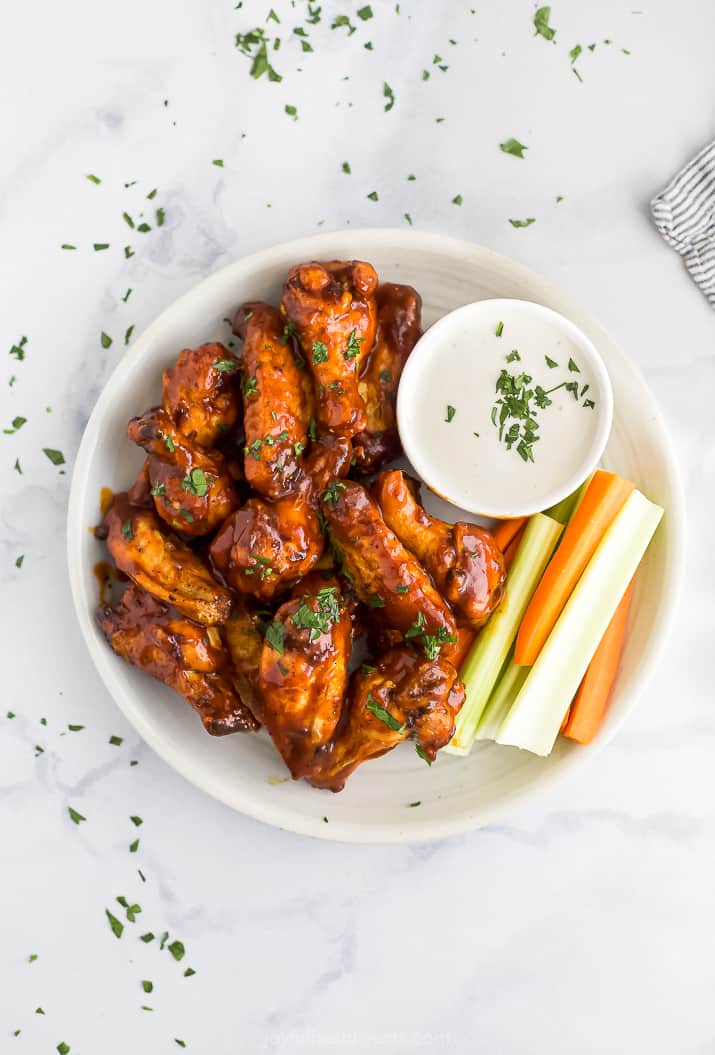 Overhead view of air fryer chicken wings on a white plate next to a side of crudités and ranch dressing.