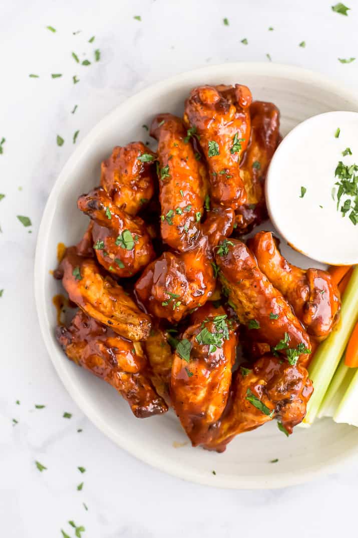 Close up overhead view of air fryer chicken wings on a white plate next to a side of crudités and ranch dressing.